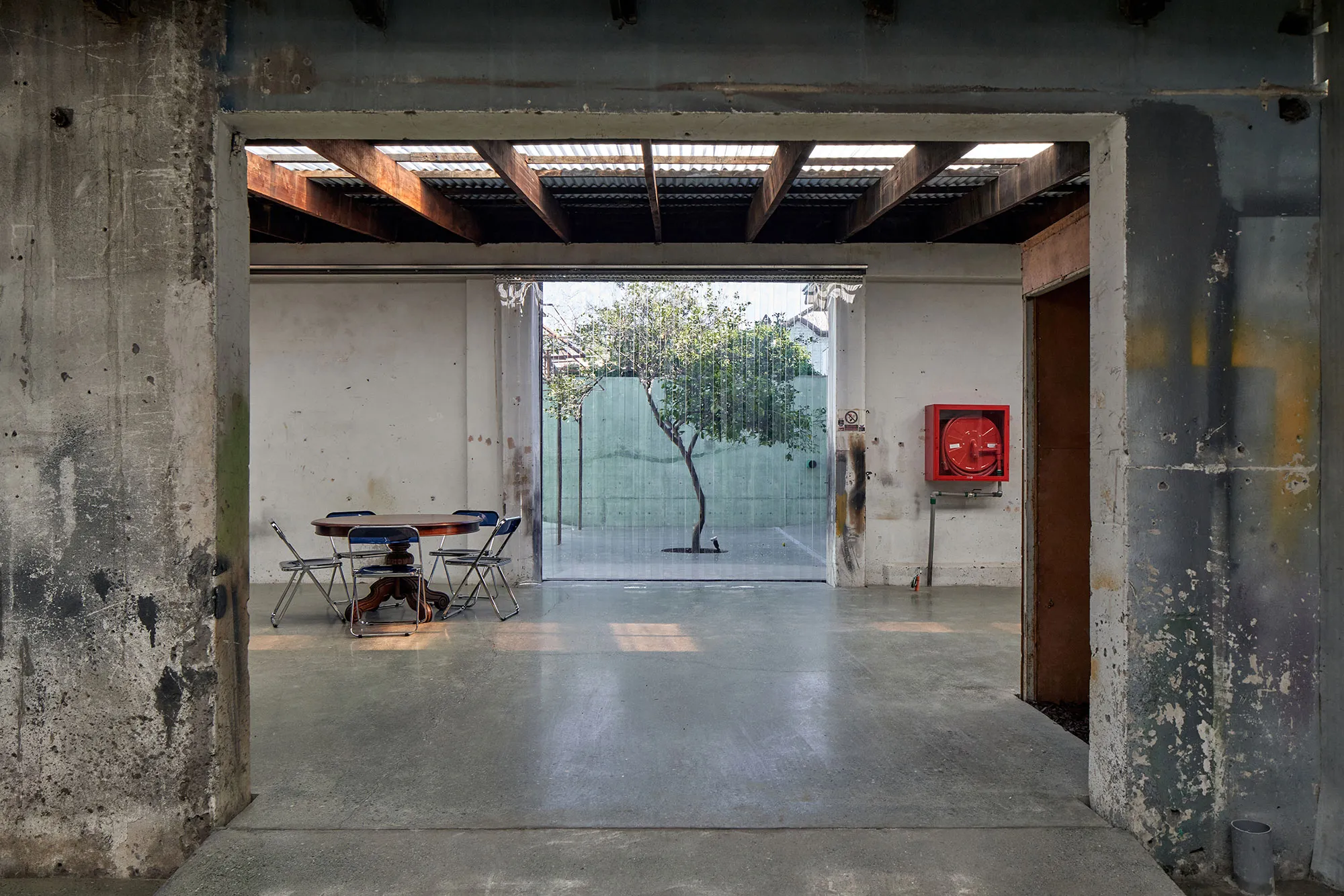 Threshold at Mestizo Barrio Italia: a concrete opening, timber beams and the courtyard lemon tree behind the curtain