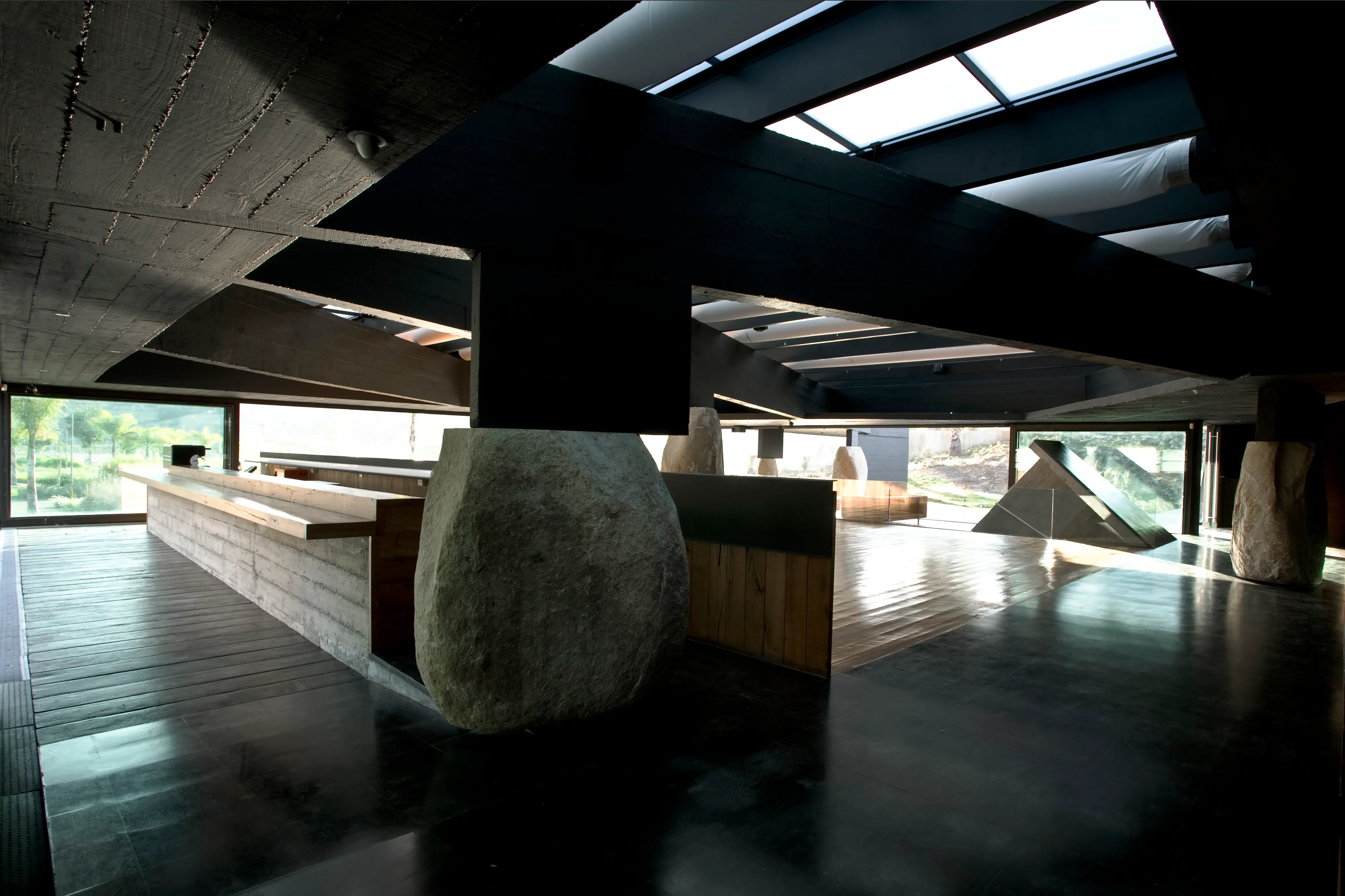 Inside Mestizo Vitacura: black concrete beams resting on river boulders, a wooden bar and windows onto the park