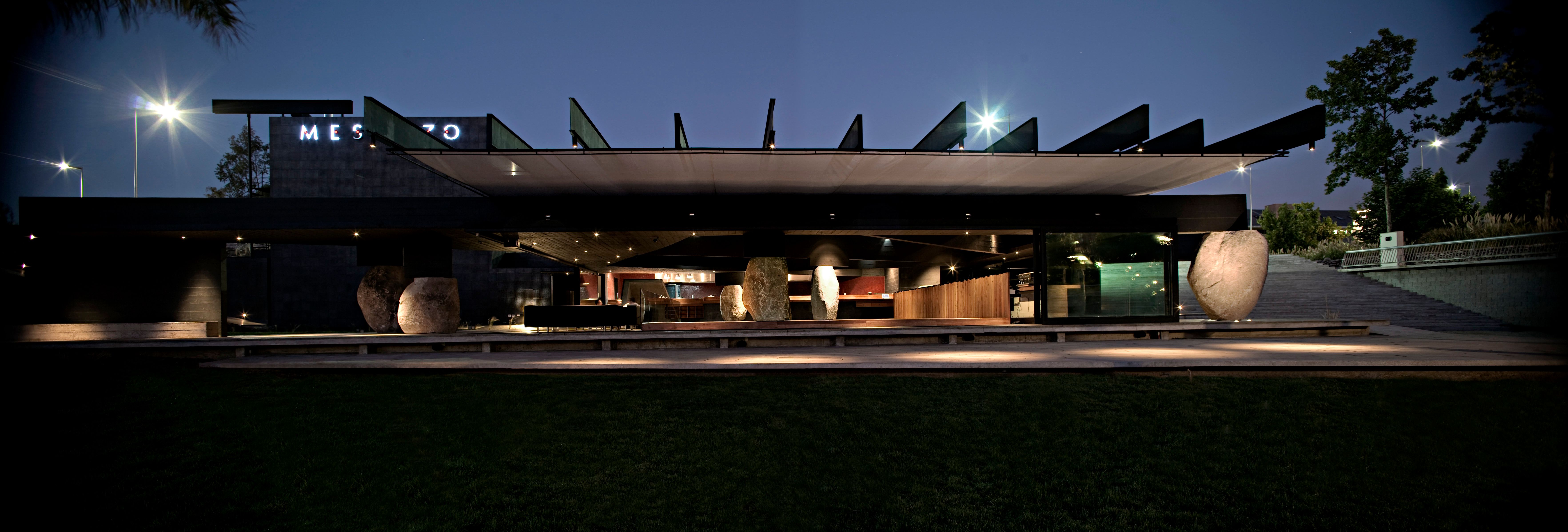 The pavilion at night: a cantilevered roof, lit river boulders and the dining room open to the park.